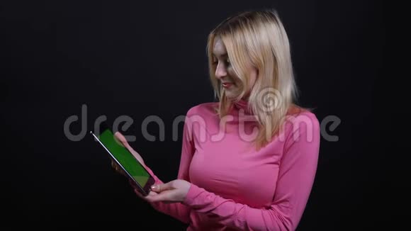 年轻漂亮的金发女性使用平板电脑的特写镜头并显示绿色彩色屏幕与背景相机视频的预览图
