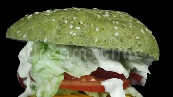 特写了一个多汁的大汉堡夹着一个撒着芝麻的绿色面包把相机从上到下旋转沿着一个视频的预览图