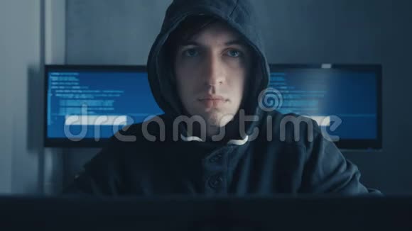 头罩中的人坐在桌子上在笔记本电脑上编码的肖像在数据中心的电脑工作的流氓视频的预览图