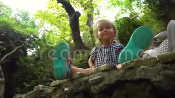 可爱的微笑女孩坐在森林里的岩石上视频的预览图