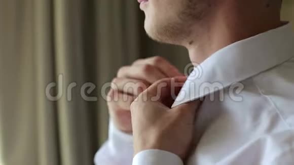 男人把他的白色衬衫扣在明亮的窗户前视频的预览图