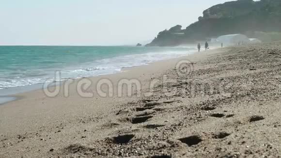 冲破海浪无法辨认的人在海上行走前景上的湿沙迹视频的预览图