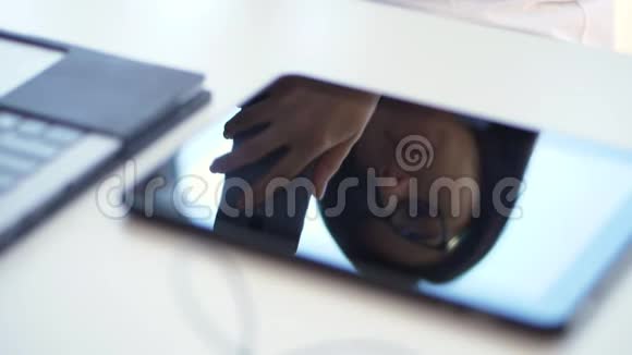 特写镜头在白色的桌面上在笔记本电脑旁边一个戴眼镜的商务女性的脸在平板电脑视频的预览图