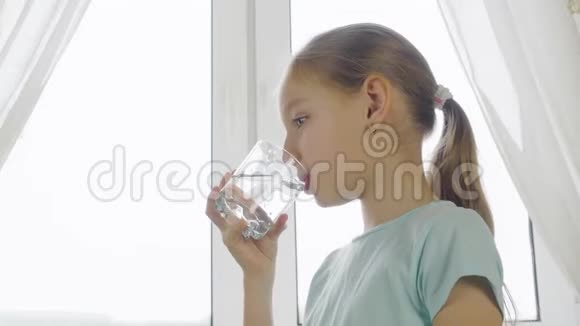 十几岁的女孩在窗前的厨房里用玻璃喝水视频的预览图