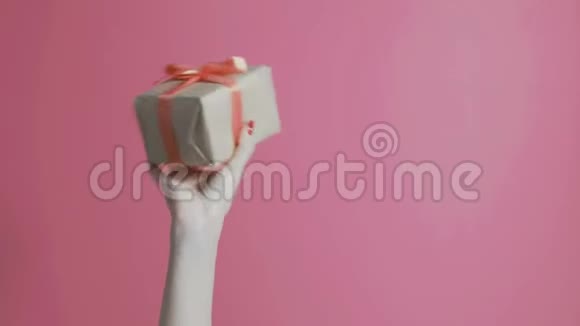 年轻女孩举起双手手里拿着一件包裹好的礼物一个女人高兴地摇着一个盒子盒子上有一个彩色的粉红色的背视频的预览图