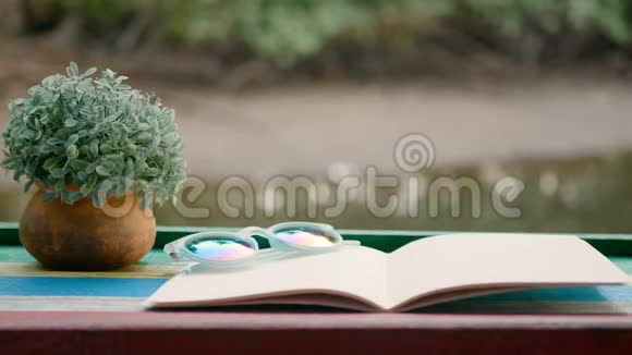 4K木桌上放着花盆放在闪闪发光的河底上的空白书的照片视频的预览图