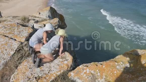 男孩们坐在悬崖边上波浪冲刷沙质海岸山脊在岩石上破碎了视频的预览图