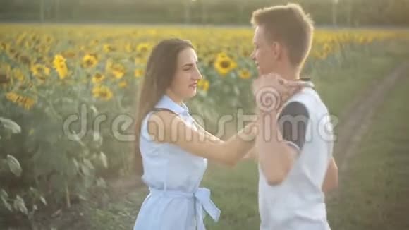一对相爱的年轻夫妇在日落时分在向日葵的田野里跳舞视频的预览图