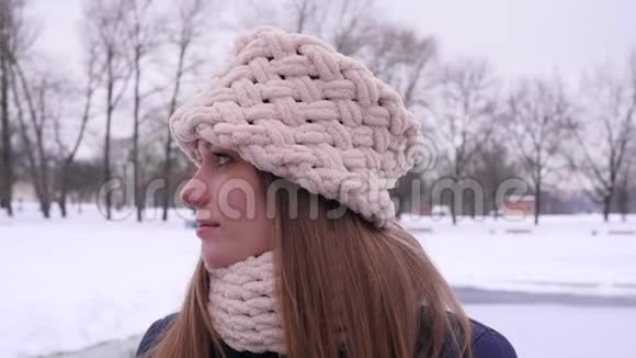 一位戴着白色针织帽子和围巾的年轻美女站在冬季城市公园里看风景的画像视频的预览图