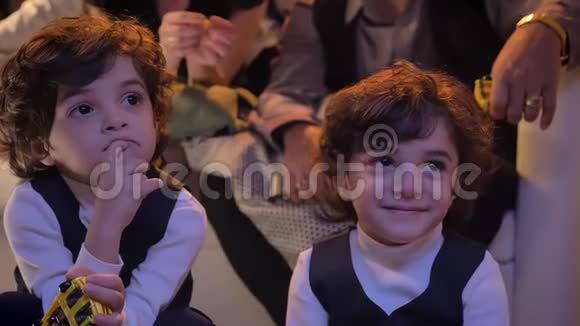 两对漂亮的阿拉伯卷头双胞胎正坐在客厅的地板上微笑着和家人一起看电视视频的预览图