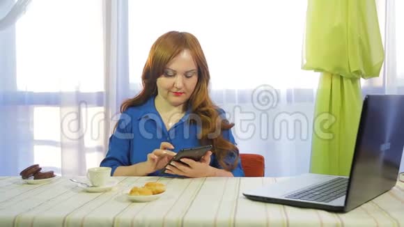 一个棕色头发的女人在一张桌子上的咖啡馆里工作拿着一块药片喝着咖啡视频的预览图