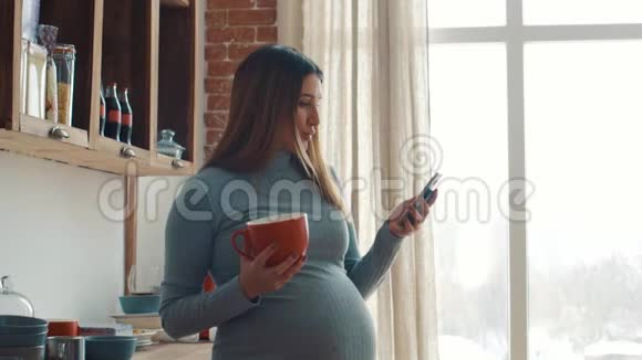 孕妇在厨房的窗户旁使用智能手机视频的预览图