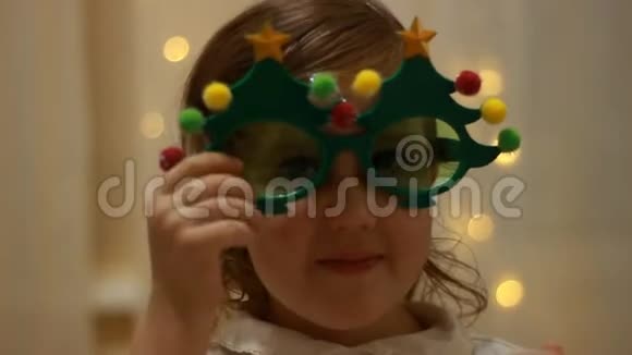 戴着太阳眼镜的小女孩带着圣诞树微笑着迎接新年一个有趣婴儿的特写肖像视频的预览图
