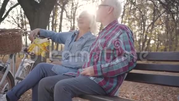 快乐的白种人退休夫妇在阳光下坐在长凳上聊天成熟的欧洲家庭阳光明媚视频的预览图