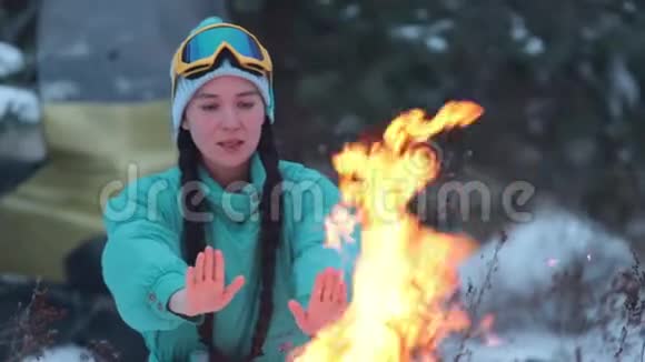 女孩温暖了她的双手在森林里的篝火上视频的预览图