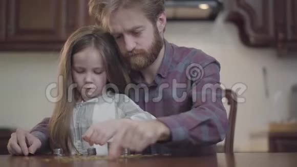 把坐在厨房桌子旁的留胡子的男人的肖像贴紧他的女儿在数钱小胡子视频的预览图