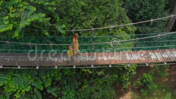 一名年轻女子和她的小儿子在丛林上的吊桥上行走的空中射击热带地区的休假视频的预览图