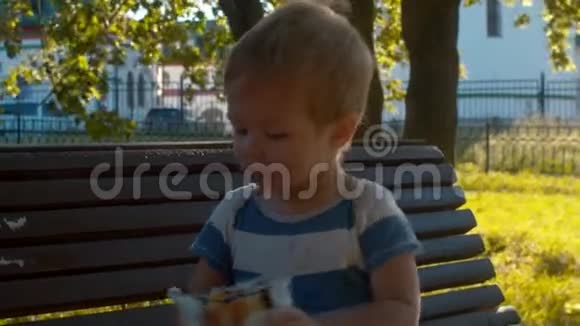坐在长凳上吃面包的小男孩视频的预览图