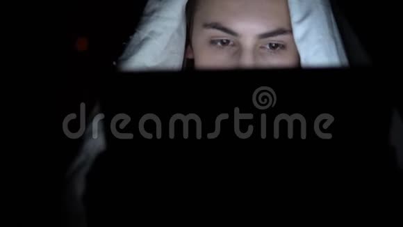 一个年轻的女人躺在毯子下面手里拿着一块药片黑暗中的女人用垫子现代电子平板电脑视频的预览图