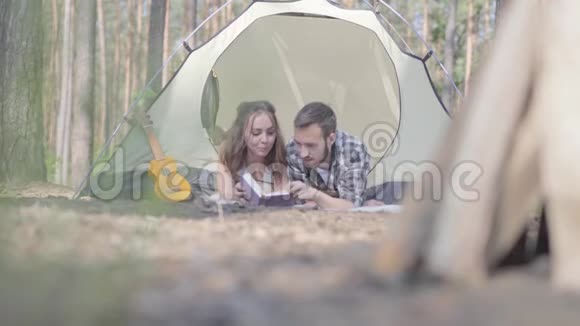 肖像年轻男子漂亮的年轻女子躺在森林里的帐篷里在看书木块视频的预览图