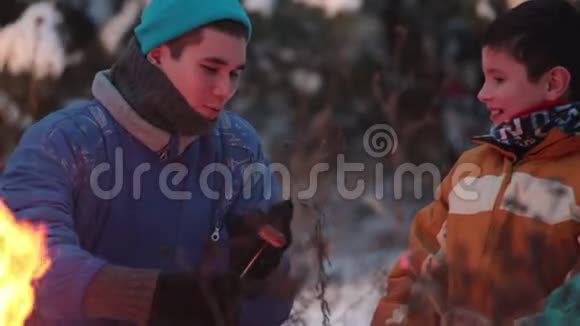 一个年轻人教他哥哥在森林里的火上煮香肠视频的预览图