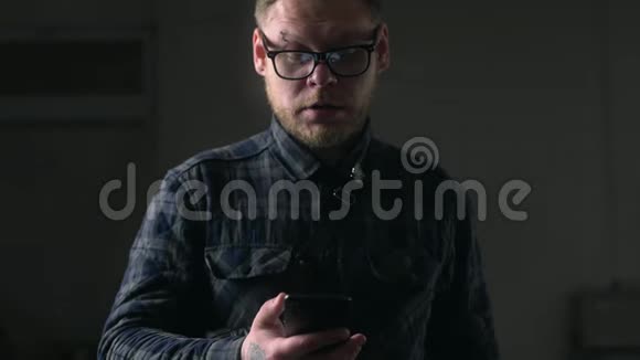 戴眼镜的人在黑暗的环境中仔细地看着他的手机拿着小玩意的人上网看着视频的预览图