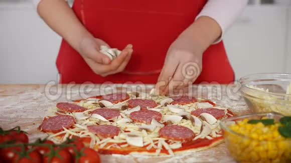 年轻女孩的手把蘑菇片和大块放在家里准备的披萨上视频的预览图