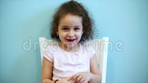 可爱的小可爱的滑稽宝宝红色卷发女孩坐在蓝色背景的白色椅子上看着视频的预览图