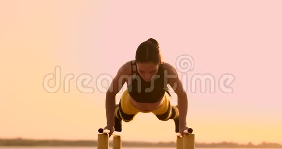 日落时分美丽的女子运动员在平行水平杆上做俯卧撑视频的预览图