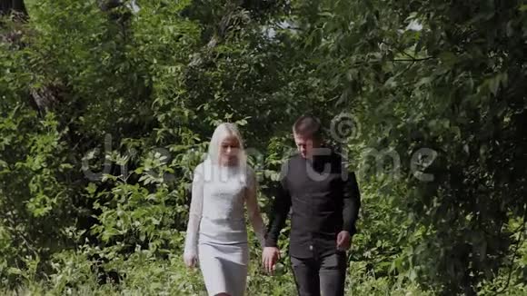 幸福的年轻夫妇相爱手牵手走在阳光明媚的森林里视频的预览图
