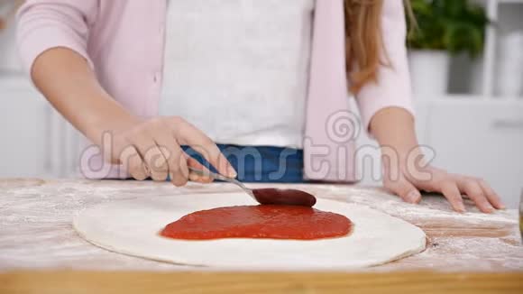 年轻女孩用手在面团上铺披萨酱视频的预览图
