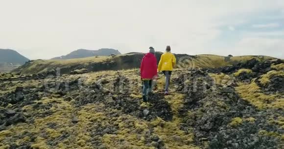 冰岛两名妇女在熔岩上行走的鸟瞰图女游客在山上徒步旅行长满了苔藓视频的预览图