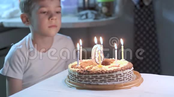 男孩坐在厨房的桌子上在生日蛋糕上吹蜡烛许愿视频的预览图