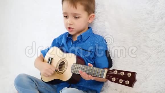 快乐的孩子坐在白色沙发上弹吉他唱歌视频的预览图