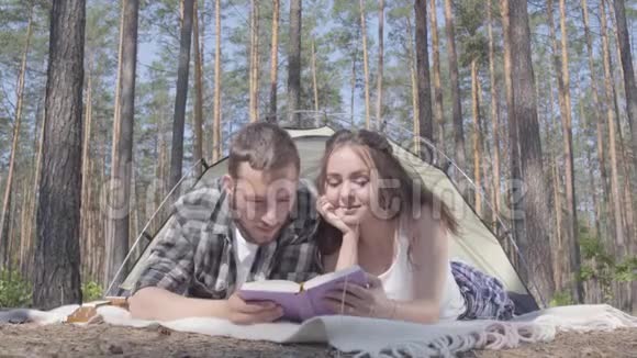 画像中的年轻人和漂亮的年轻女人躺在森林里的帐篷里看书爱视频的预览图