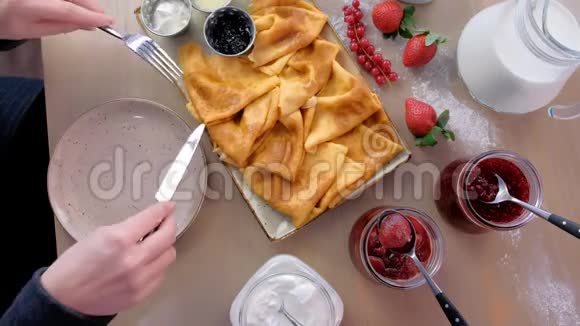 女人正在吃俄罗斯传统的薄煎饼在盘子里放上果酱酸奶油和草莓特写视频的预览图