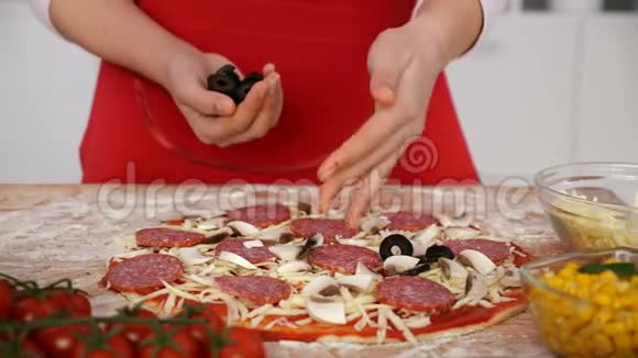 年轻女孩把橄榄片撒在家里准备的披萨上视频的预览图