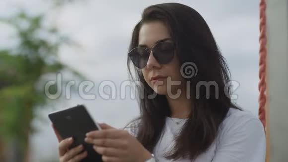 戴墨镜的美女在户外看电子书视频的预览图