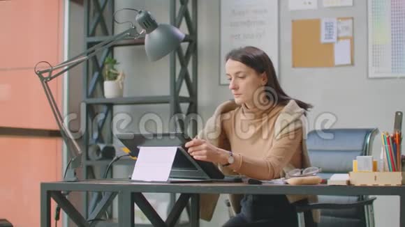 一位女平面设计师在一间有大窗户的办公室工作用手写笔和电脑触摸屏作画视频的预览图