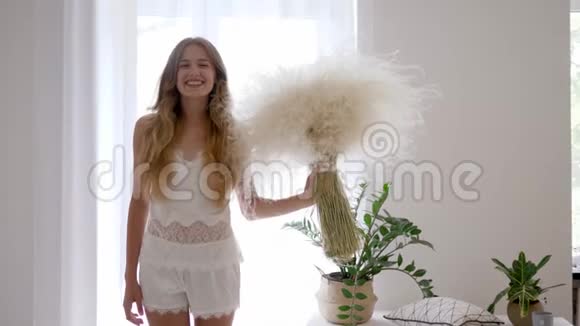 睡衣的快乐女孩站在家里手里拿着一束羽毛草无过敏视频的预览图