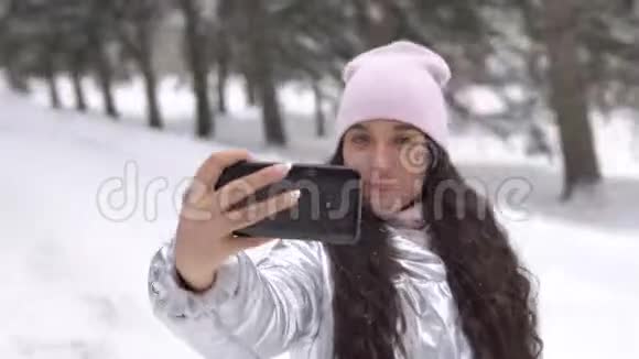 迷人的女孩在冬天的森林里站着用智能手机自拍4K视频的预览图