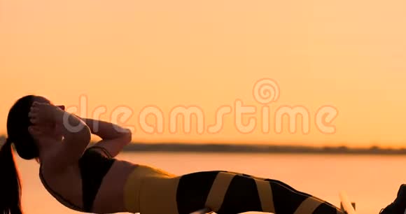 腹部肌肉锻炼日落时分一位年轻的美女在湖边运动一位穿着运动服的夏日女子在做运动视频的预览图