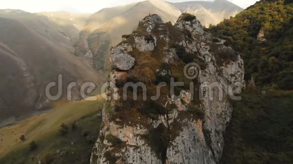 一个年轻人坐在山上岩石上的莲花位置上沉思空中观景航班视频的预览图