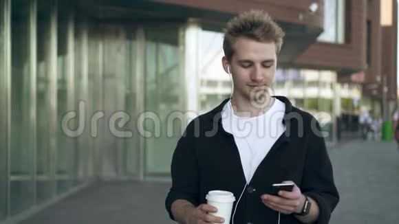 带智能手机和咖啡听音乐的微笑青年的正面景色视频的预览图