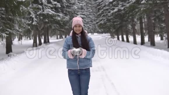 心情好的漂亮女孩站在冬天的森林里微笑着用手吹雪慢速高清视频的预览图