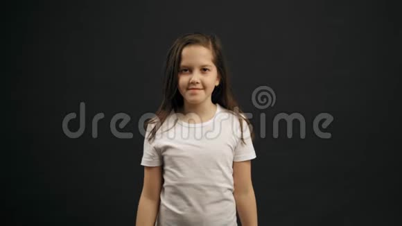 小女孩的肖像是用她的手显示心脏微笑着看着相机黑色背景视频的预览图