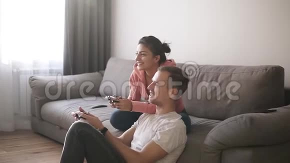 情绪化的年轻夫妇在家玩电子游戏坐在沙发上男人在地板上享受在一起玩的时光视频的预览图