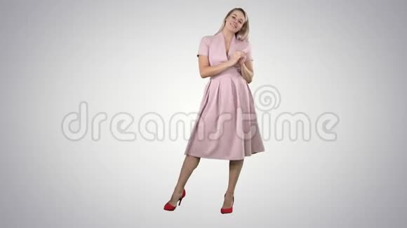 快乐的金发女人穿着粉红色与相机交谈并指向侧面的渐变背景视频的预览图