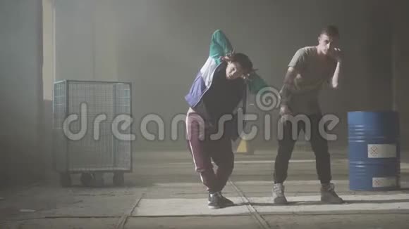 两个年轻人在废弃建筑的黑暗和尘土飞扬的房间里跳舞做舞蹈动作和姿势的人看视频的预览图