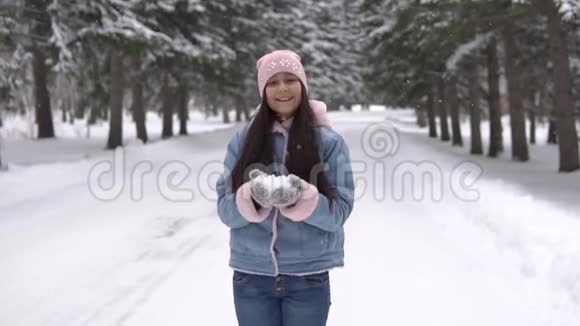 心情好的漂亮女孩站在冬天的森林里用手吹雪视频的预览图